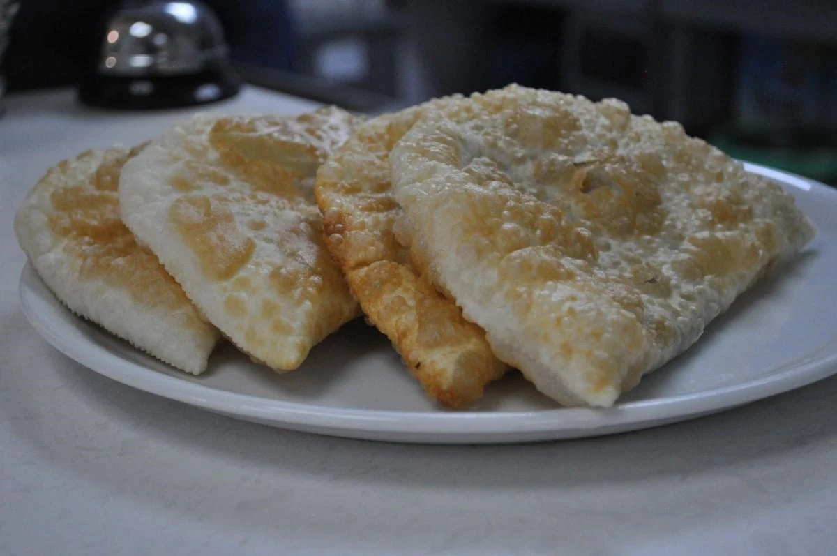 Bazı kelimelerde güncellemeye giden Türk Dil Kurumu'nun (TDK) 'Çiğ börek' yazılışını'Çi börek' olarak değiştirilmesini değerlendiren Eskişehirli esnaf ve vatandaşlar, değişiklik kararının isabetli olduğunu ifade etti.
TDK, Türkçede 18 kelimenin yazımında değişikliğe gitti. Yazımı değişen kelimelerin arasında Eskişehir’in yaygın lezzetlerinden olan Çi börek de bulunuyor. Yapılan yeni değişiklikle birlikte bu lezzet Çiğ börek artık Çi börek olarak kullanılacak. TDK’nın bu son güncellemesin ardından Eskişehirli Çi börek esnafı hazırlıklar yapmaya başladı. Çi börekçiler TDK’nın kelime güncellemesini olumlu karşılarken, işletmelerinin tabelalarını da son değişikliğe göre ayarlayacaklarını söyledi. Bazı vatandaşlar da güzel börek manasına gelen çi börek kelimesindeki güncellemenin yerinde bir karar olduğunu ifade ederek günlük hayatta fazla kullanılan diğer kelimelerde de düzenlemeler yapılabileceği şeklinde görüş belirtti.

“Doğru olan yazılış çi börek”
35 yıllık çi börek ustası Necati Aslan, TDK’nın değişiklik kararını doğru bulduğunu belirterek, “Önceden halk dilindeki yazılımı çiğ kelimesinden esinlenerek çiğ börek olarak koyulmuş. Yıllarca öyle devam etmiş. Daha sonra Türk Dil Kurumu, yumuşak G’yi koymadan onun yerine çi börek kullanıldı. Çi börek lezzetli börek anlamına geliyor. Doğru olan yazılış çi börek. Yumuşak g’siz çi börek. Çi, ayrı bir kelime. Tabeladaki yazıyı da ileride düzelteceğiz. Eskiden beri halk çi börek olarak algılıyordu. Günümüzde de artık kelimeler TDK’ya göre ayarlandığı için çi börek kullanılmaya başlandı. Doğru olan da bu” diye konuştu.

“Kısa yoldan çi börek demek daha iyi”
Bir başka çi börek ustası Hasım Kara ise böreğin Tatarca’daki asıl adının farklı olduğunu savunarak, “Esasında böreğin ismi ne çiğ börek ne çi börek. Tatarca’da böreğin esas ismi şığ börek. İyi börek, güzel börek anlamı. Nasıl yazın derlerse öyle yazılır. Bizim için sorun olmaz. Ben Eskişehirli değilim, buraya geldiğimde öğrendiğim çi börek diyordu herkes. Ama sordum öğrendim aslı şığ börek. Müşterilerden soran olursa şığ börek diyorum. Kısa yoldan çi börek demek daha iyi. Her yerde çiğbörek diye geçiyordu. Ne yazarsak yazalım, gelenler ‘çi börek yemeye geldik’ diyorlar” dedi.

“Çi börek olarak söylemek daha hızlı ve kolay”
Vatandaşlardan İbrahim Şener de çi börek kelimesindeki gelişmenin hızlı ve kolay söylenmesi açısından faydalı olduğunu dile getirdi. Bu değişikliklerin kelimelerdeki karışıklığı ortadan kaldıracağını düşünen Şener, “Yumuşak g’nin kaldırılması dilimizin sadeleştirilmesi, kelimelerin daha kolay söylenmesi bakımından aslında faydalı bir gelişme olmuş. Çi börek olarak söyleme şekli de daha hızlı ve kolay. TDK’nın bu yaptığı çok isabetli bir karar olmuş. Kelimenin hem kısaltıldı hem de aslına dönmüş oldu. Bu kurallar aslında olması gerektiği gibi standartlaştırılıyor. Karışıklığı engellemek açısından standartlaştırılması bence mantıklı. Tabelalardaki değişiklikler de bu kelimenin halka yansıması ve daha kolay söylenmesi açısından faydalı olacak. Bir kelimenin farklı şekillerde söylenmesindense ortak bir kelime üzerinden herkesin aynı şekilde o kelimeyi kullanması hem Eskişehir için faydalı hem de kafa karışıklığını ortadan kaldırıyor. Bu şekildeki çalışmalar sadece çi börek’te değil günlük olarak fazla kullanılan kelimelerde de olması gerekiyor. Çünkü dilimizde çok fazla kullanılan yabancı kelimeler var. Dilimizin hem bozulmaması hem sadeliğini koruması açısından bunun TDK tarafından yaygınlaştırılması gerekiyor” dedi.

Çi börek nedir ve nasıl yapılır?
Aslı Tatarlara dayanan Eskişehir’e göç eden Kırım Tatarlarına özgü lezzetlerden olan Çi börek, güzel ve iyi börek anlamına geliyor. Un, tuz, su ve kıymanın karışımıyla yapılan çi börek için önce orta büyüklükte bir hamur açılıyor. Bu hamurun içine kıymalı harç ile doldurulup kapatılıyor. Daha sonra içi dolu hamurlar yarım ay şeklinde kesilerek kızgın yağlı kazana atılıyor. Birkaç dakika yağın içinde kızartıldıktan sonra tabaklara servis ediliyor. Çi börek ustaları böreği kazandan çıkartıldıktan sonra tazeliğinin bozulmaması adına sıcak bir şekilde yenmesini tavsiye ediyor.